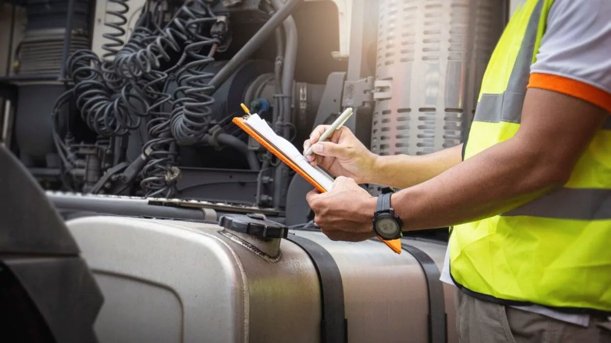 Truck inspector in a safety vest filling out an inspection checklist beside a semi-truck