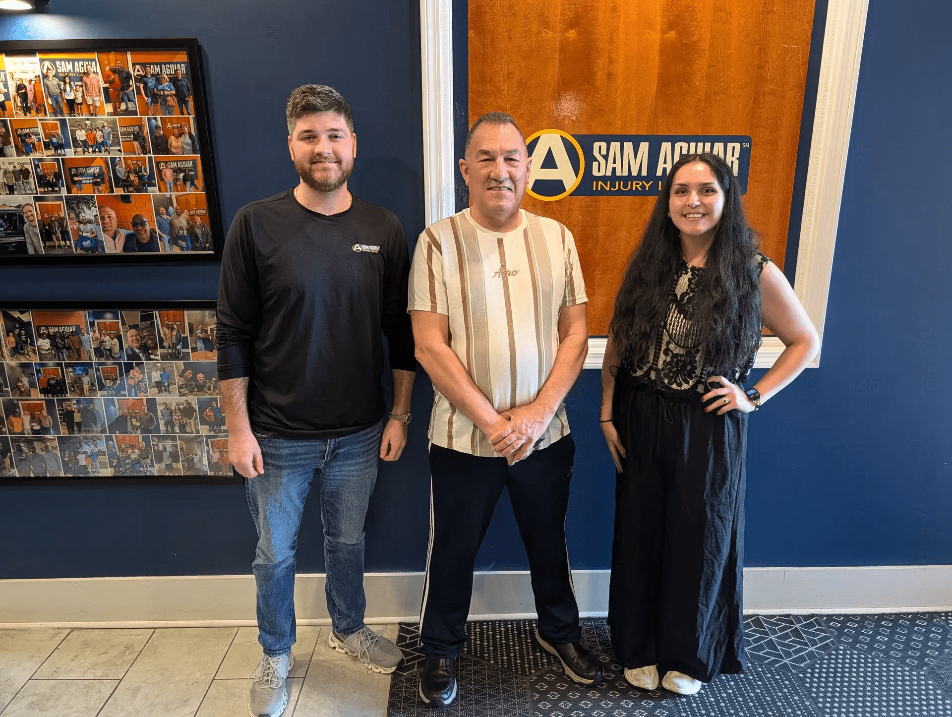 Two Sam Aguiar Injury Lawyers team members standing with a client in front of the firm’s logo