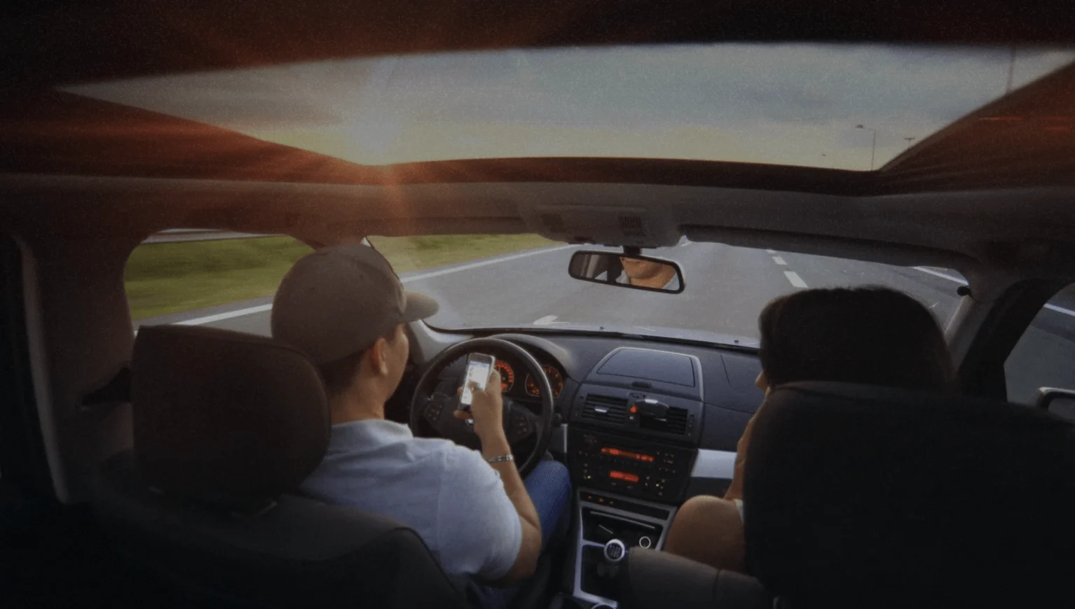 Driver holding a phone at the steering wheel on a highway while a passenger sits beside him