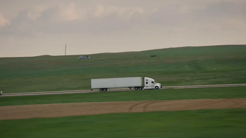 White 18-wheeler crossing open grassland on a two-lane highway