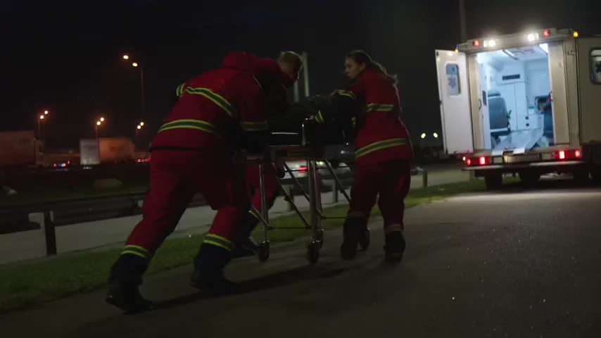 Paramedics rolling a patient on a stretcher toward an ambulance at night