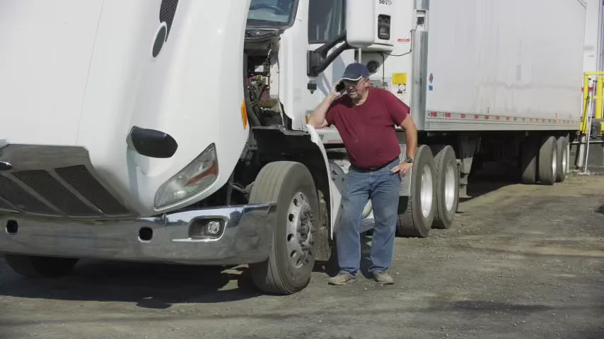 Truck driver on the phone beside a semi with its hood tilted open