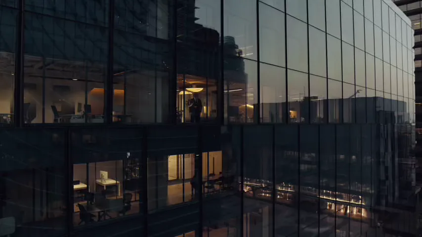 Glass office tower at dusk with lit floors of corporate offices