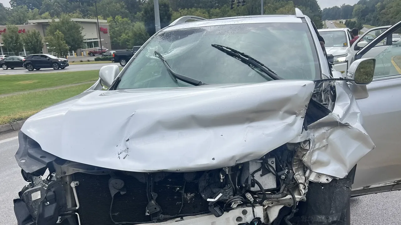 Silver SUV with a crushed hood and broken windshield stopped on a road beside other traffic