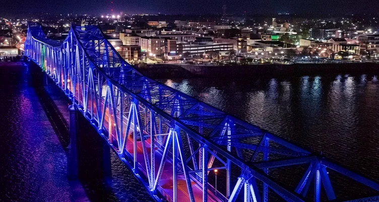 The Glover Cary Bridge lit blue at night over the Ohio River, with downtown Owensboro beyond