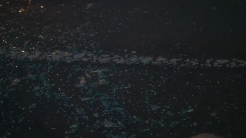 Broken glass and vehicle debris scattered across a roadway at dusk
