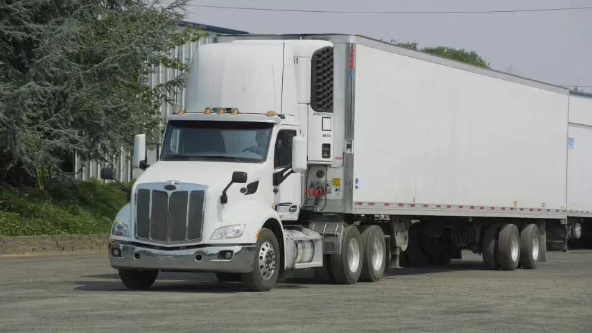 White refrigerated tractor-trailer pulling forward through a gravel yard