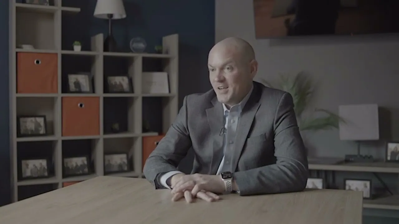 Sam Aguiar leaning on a table while speaking in a firm office